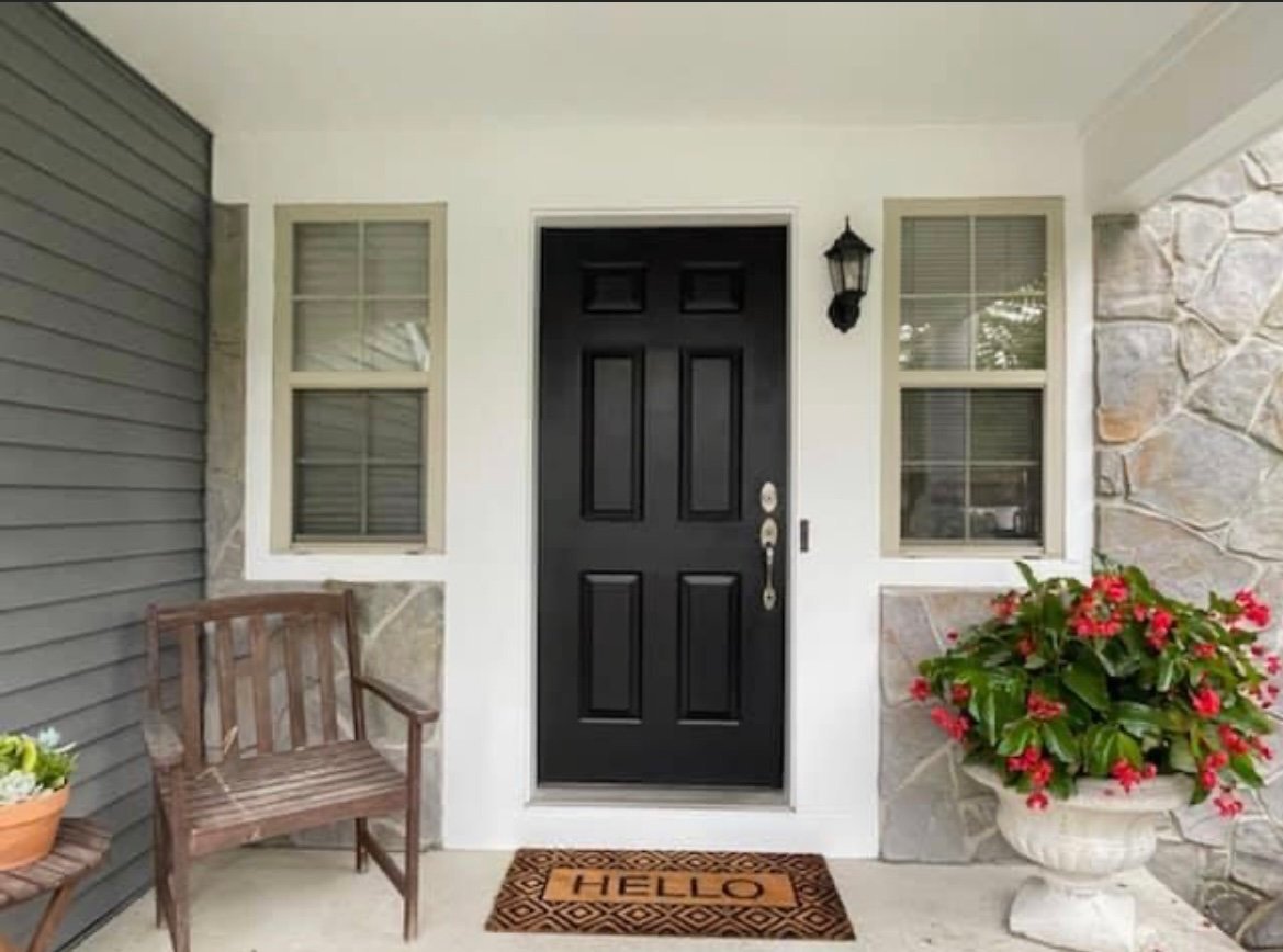 Front entry with a black door, stone, and gray siding