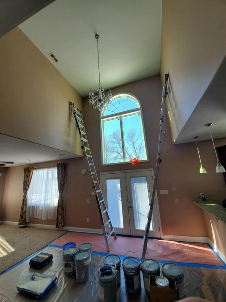Tall ladders set up in a two-story interior, floors fully covered before painting